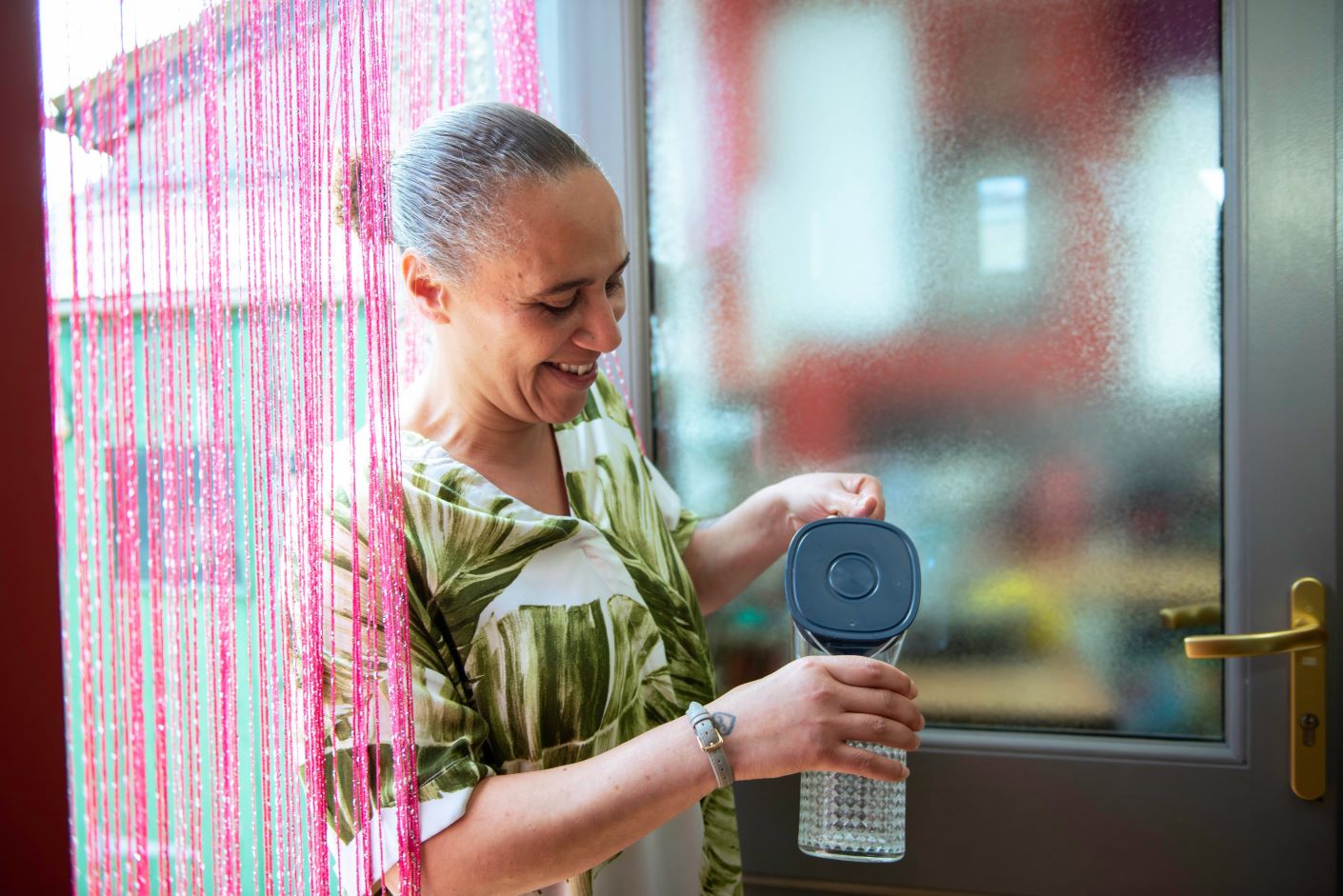 Woman in the front door of her home, smiling and pouring water from a jug